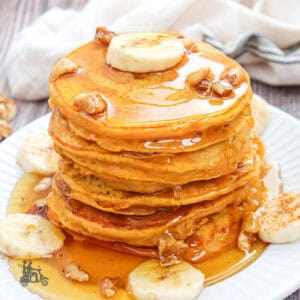 A high stack of banana pumpkin muffins with sliced bananas and maple syrup over the cakes.