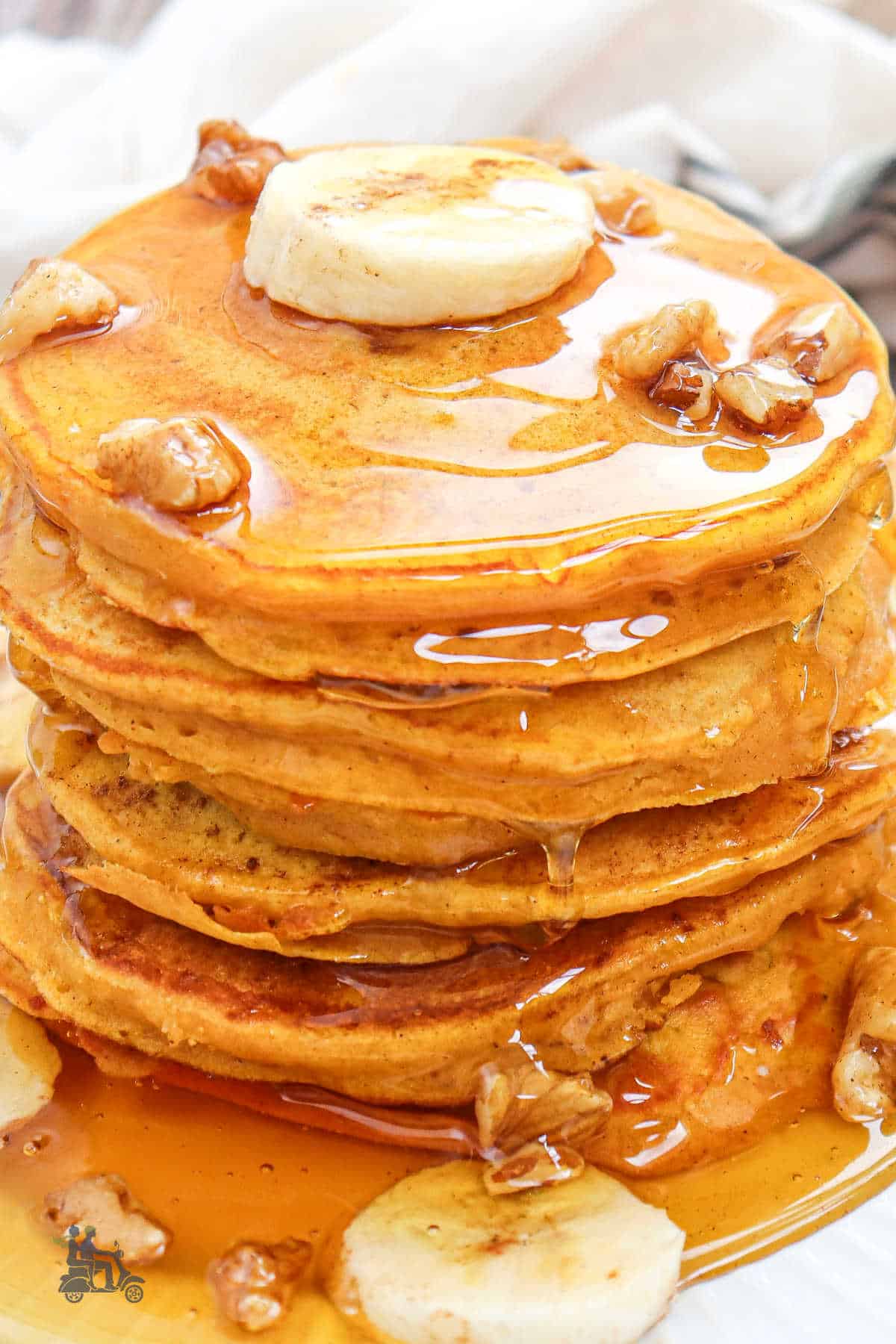 Pumpkin banana flatcakes stacked on a white plate with maple syrup poured over them. 