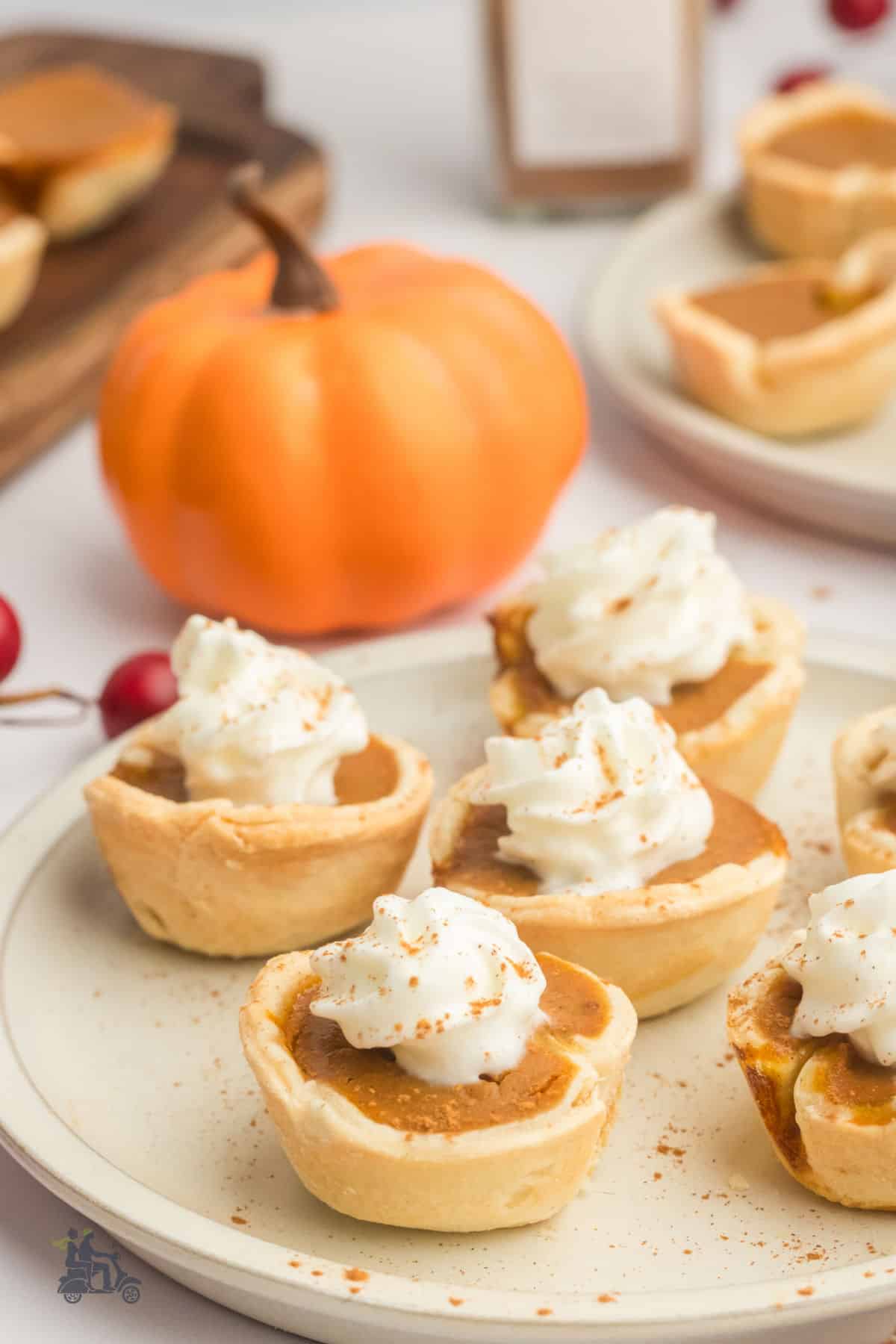 An Autumn themed table set with an orange pumpkin and a plate with six mini pumpkin pies. 