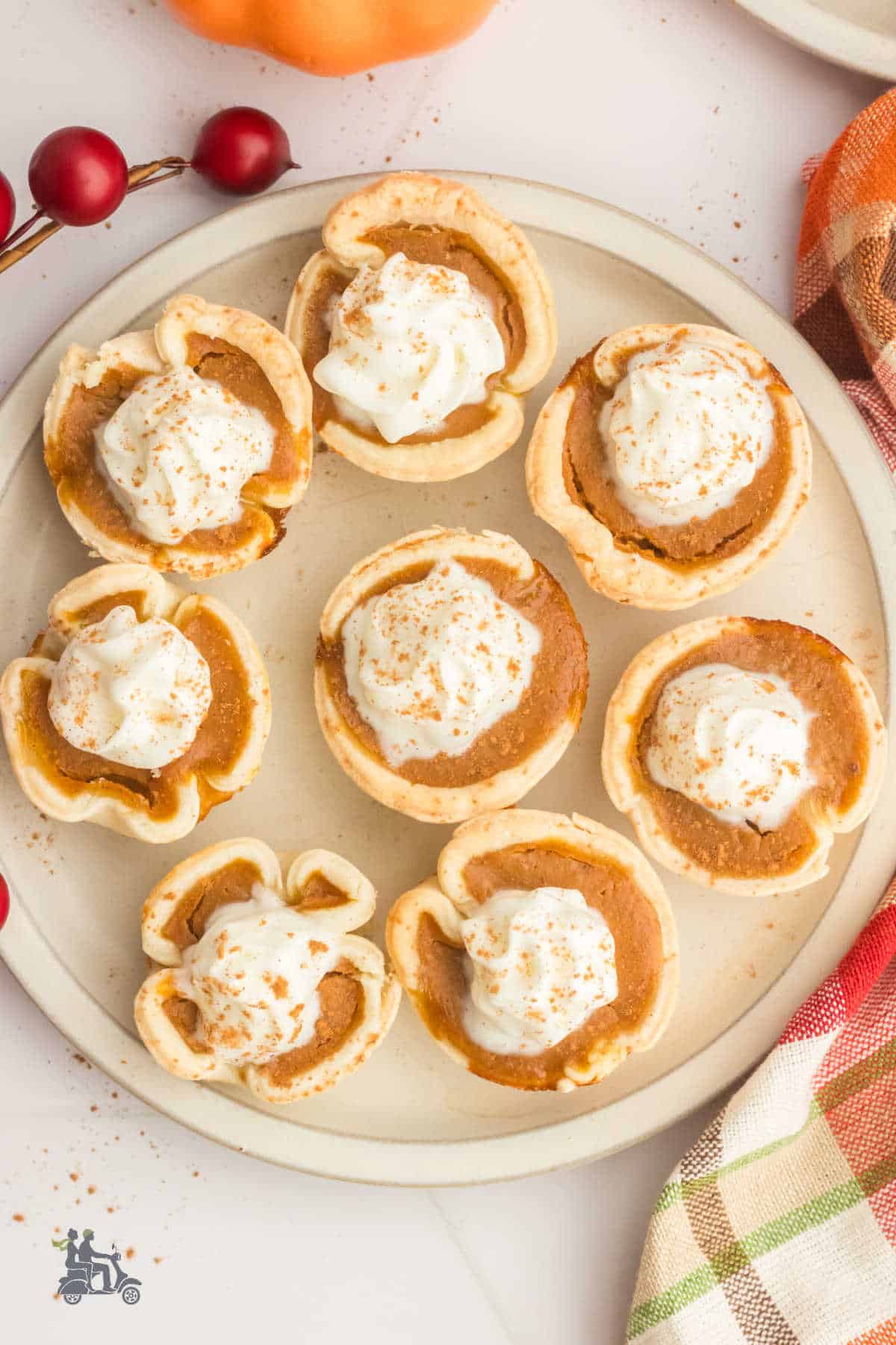 Individual pumpkin pies topped with sweetened whipped cream are on a cream dessert tray ready to serve. 