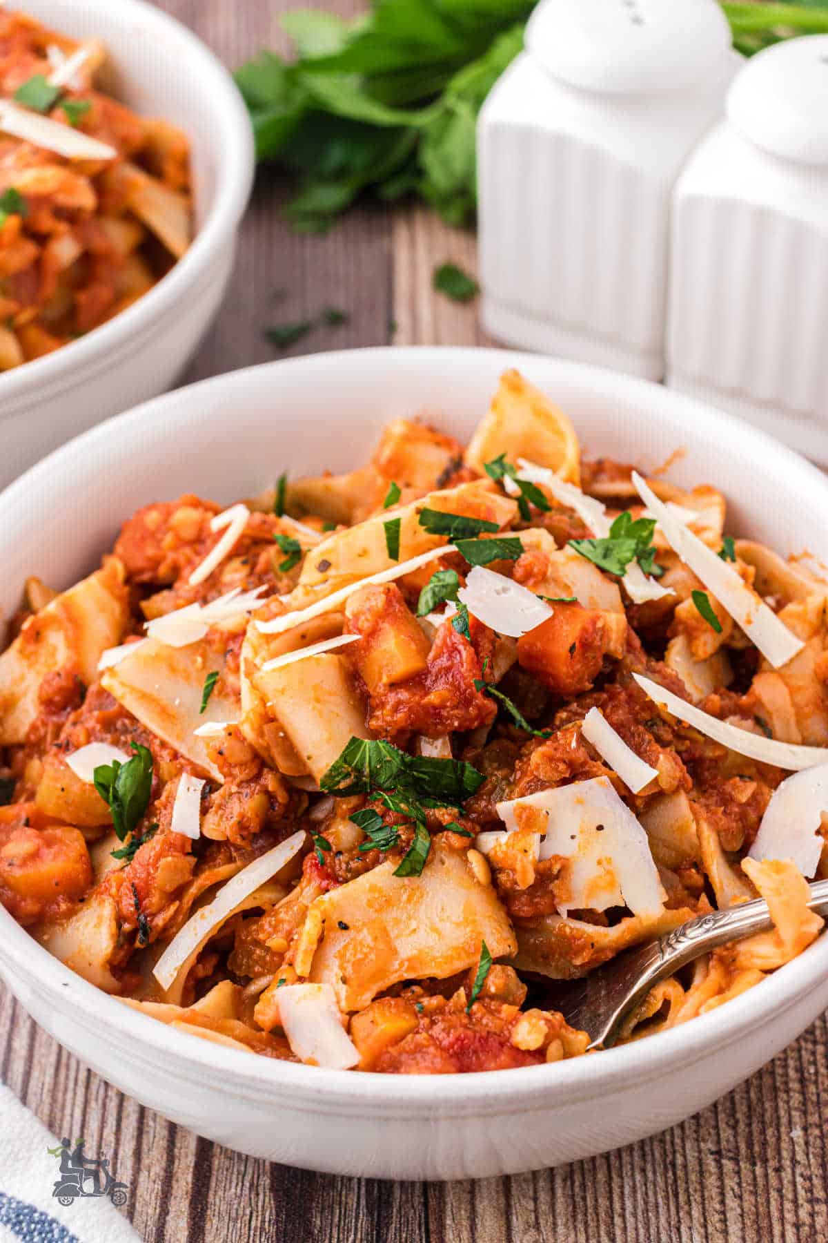 A white pasta bowl holds a heaping helping of vegetarian lentil sauce tossed with tender pasta ribbons. 