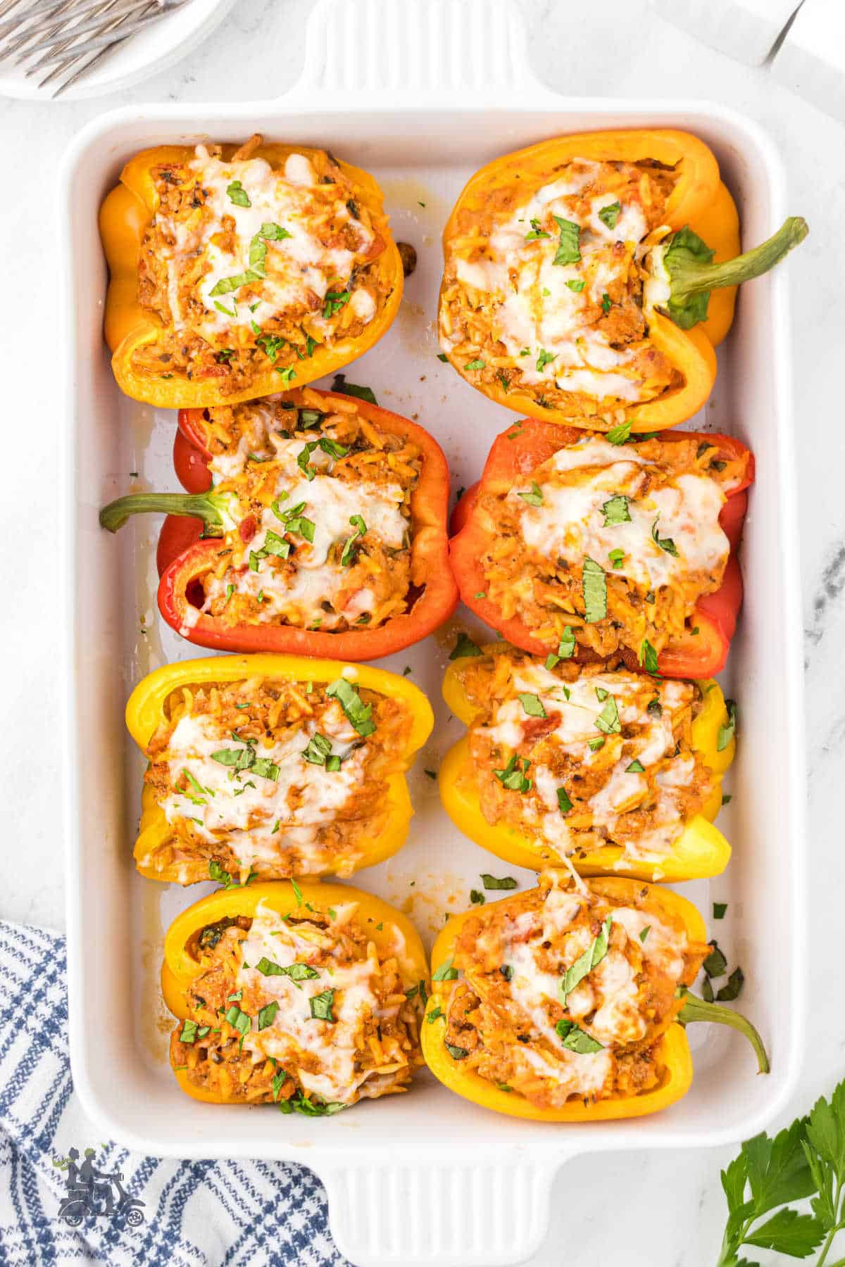 A white casserole dish holds eight turkey sausage and orzo pasta-stuffed bell peppers, oven-baked until the cheese is melted. 