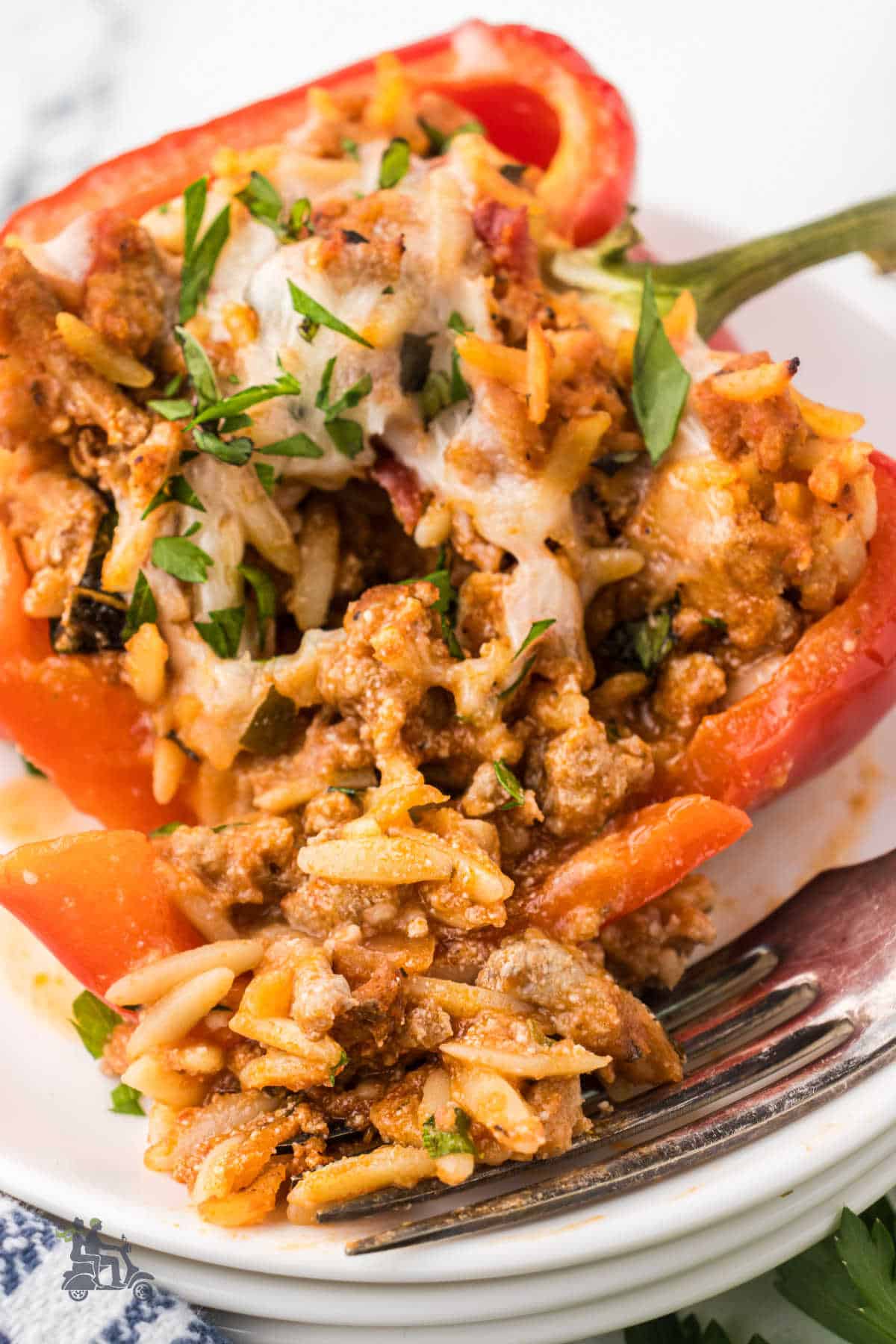 Red bell pepper is filled with sausage and pasta mixture with a fork on the side. 