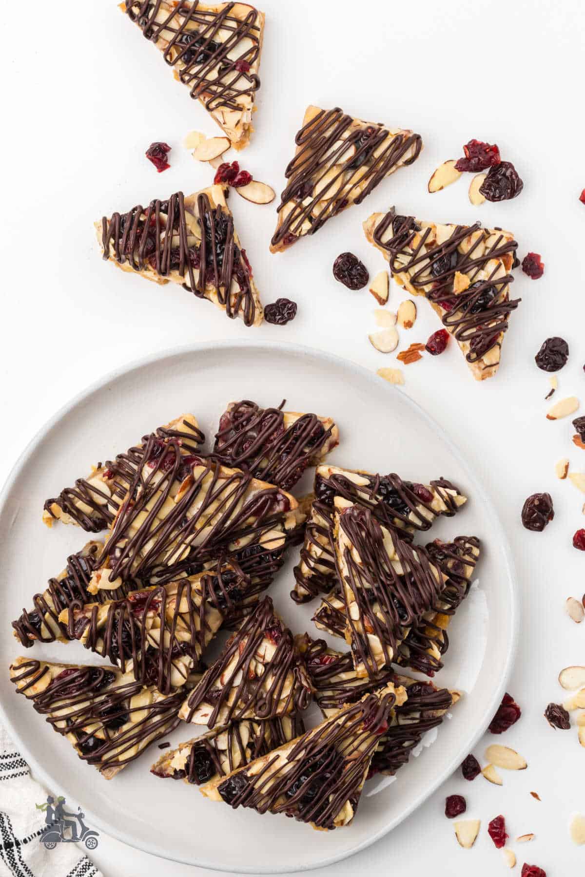 Italian Florentine cookies with nuts and mixed fruit fill a white plate and are scattered on a white counter. 