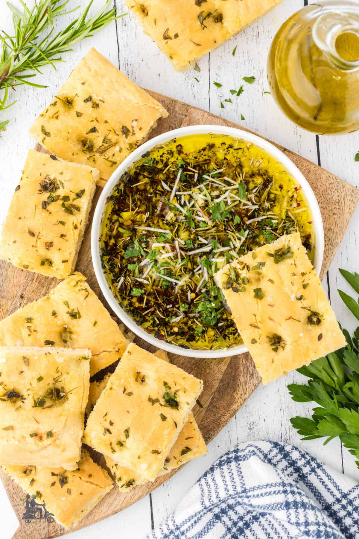 Bread dipping oil with garlic and herbs in a white bowl surrounded my focaccia squares. 