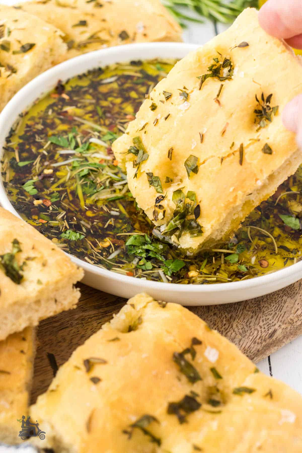 A square of focaccia bread is dipped into garlic olive oil bread dipping sauce. 