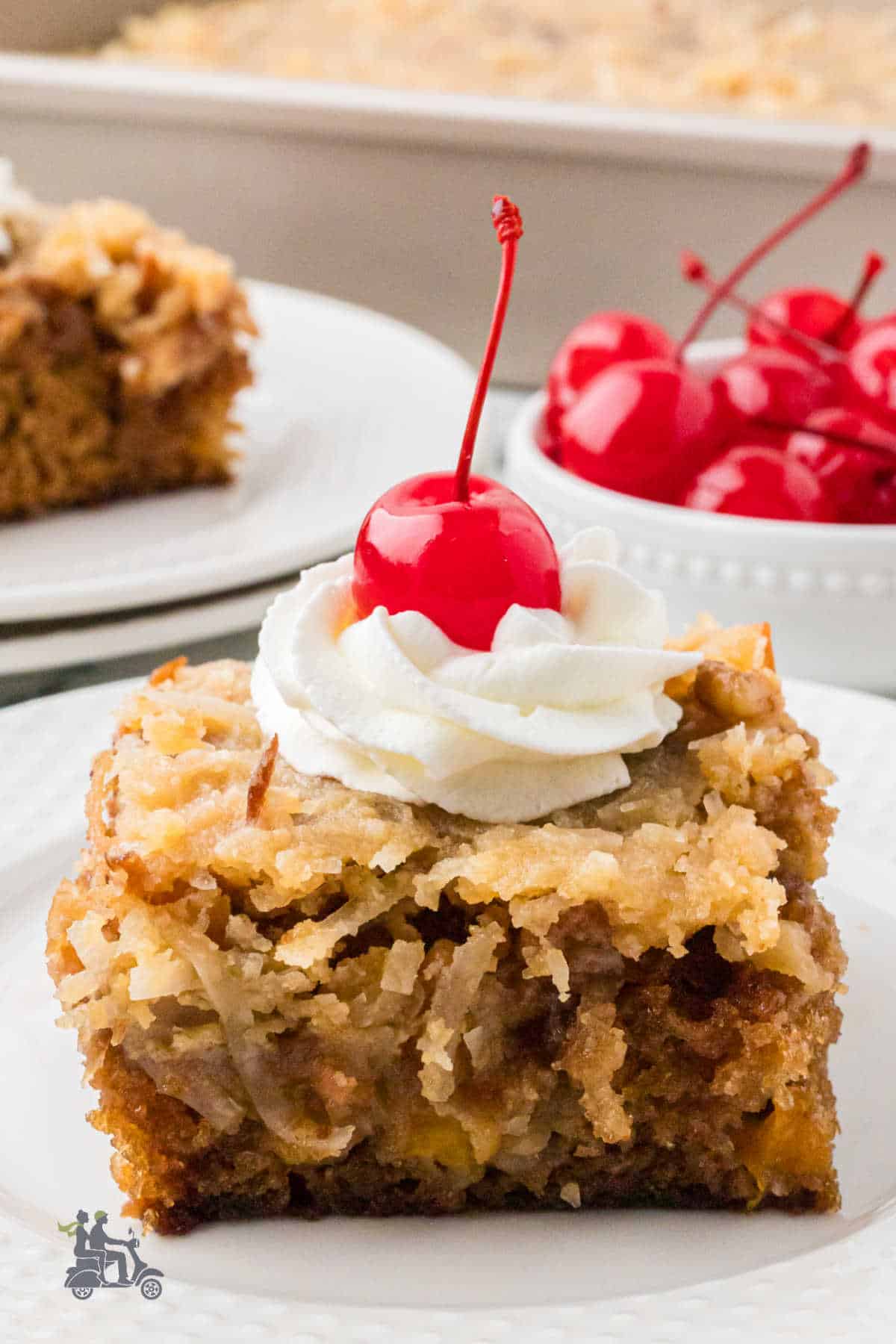 A favorite potluck dinner dessert square of classic fruit cocktail cake with whipped cream and a cherry on top.