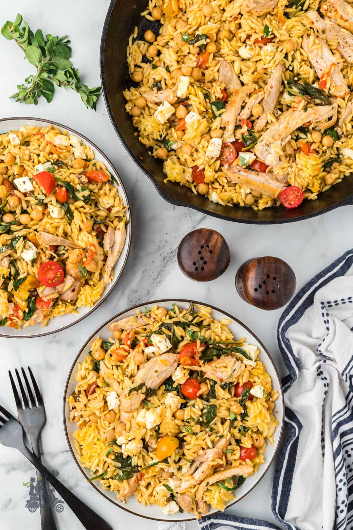Two white bowls filled with Mediterranean chicken thighs, Feta cheese, and lemon orzo pasta. 