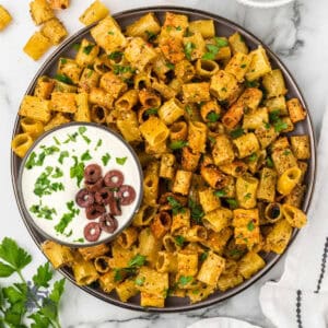 A bowl of pasta chips seasoned and sprinkled with Italian parsley and a Mediterranean feta dip on the side.