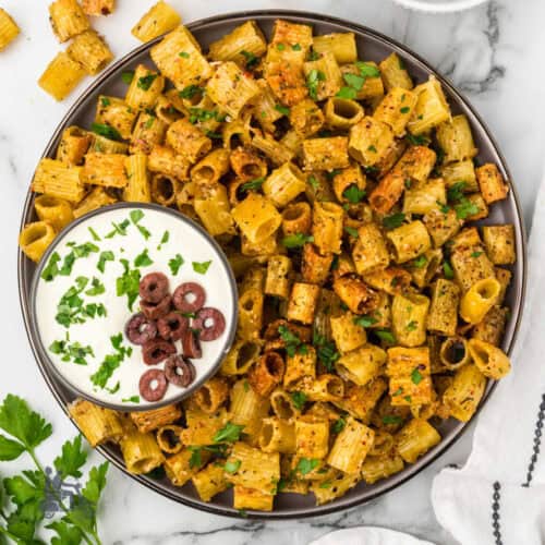 A bowl of pasta chips seasoned and sprinkled with Italian parsley and a Mediterranean feta dip on the side.
