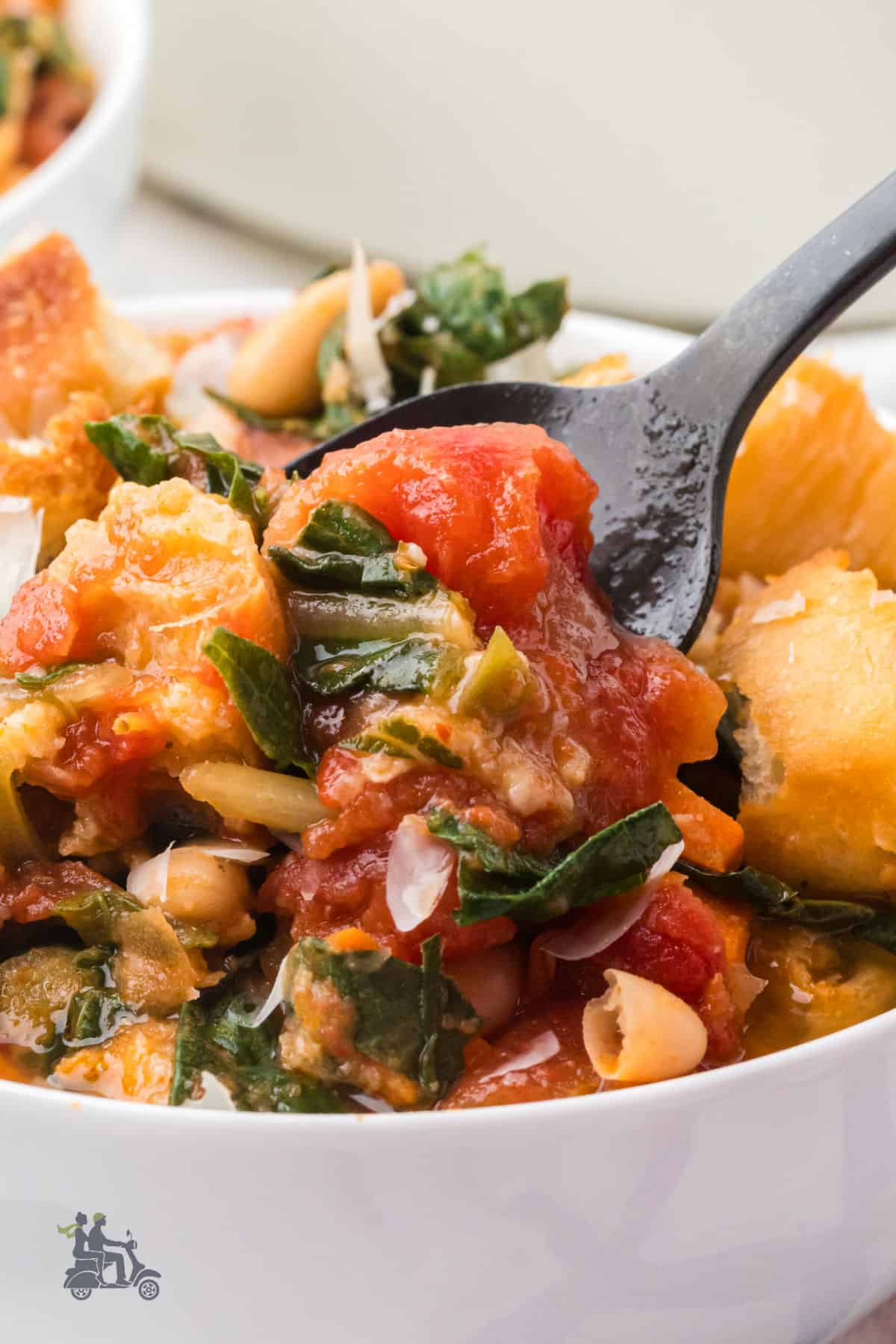 A black spoon dips into a bowl of Italian bread soup. 