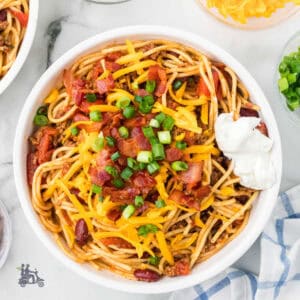 A white bowl filled with western-style spaghetti and topped with sour cream and green onions.