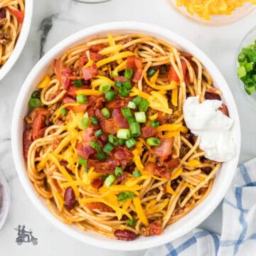 A white bowl filled with western-style spaghetti and topped with sour cream and green onions.