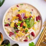A white bowl filled with creamy poblano chicken soup topped with corn chips and chopped cilantro leaves.