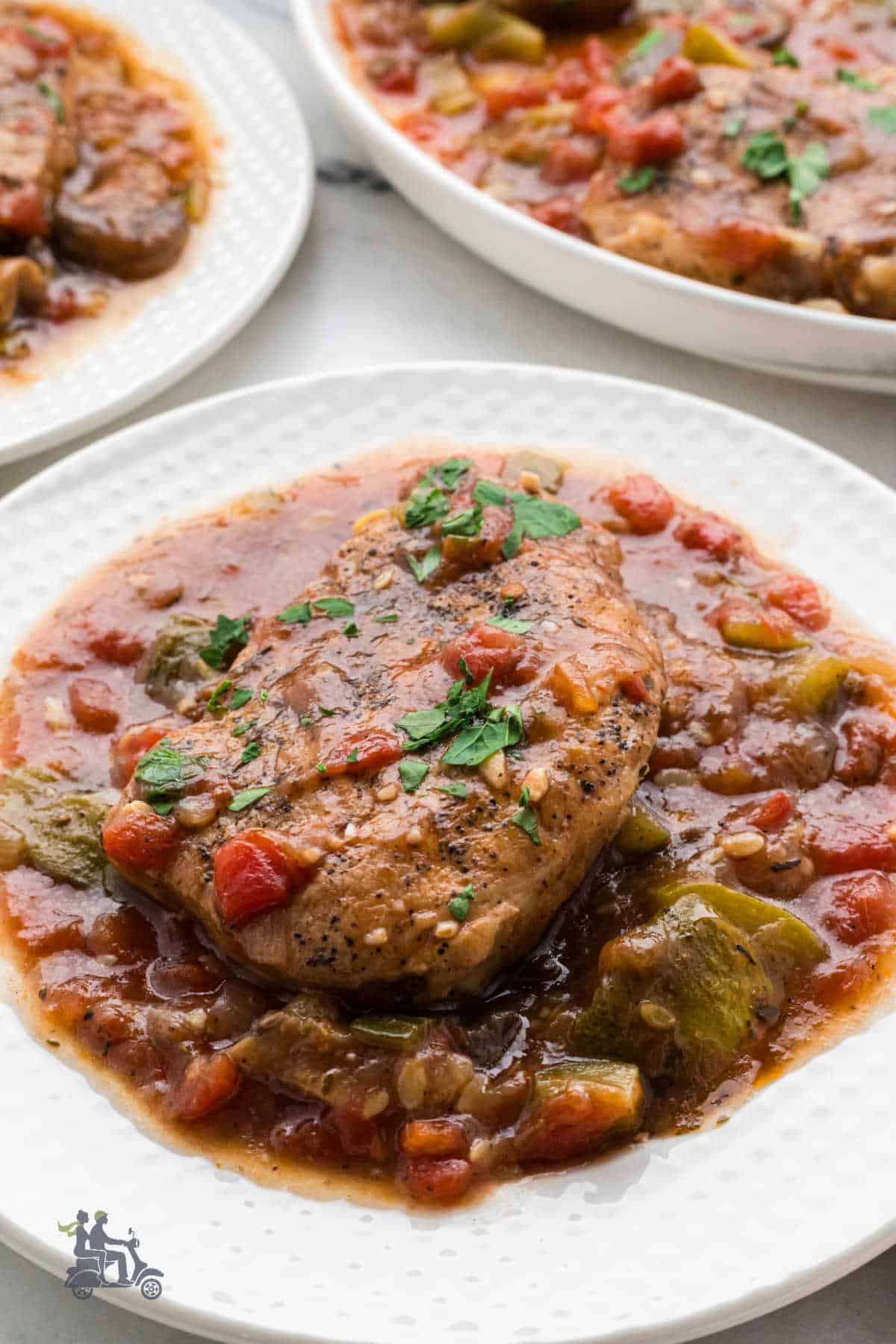 Italian Pork Chops with vegetables, sauce, and a sprinkle of Italian chopped parsley on a white plate.