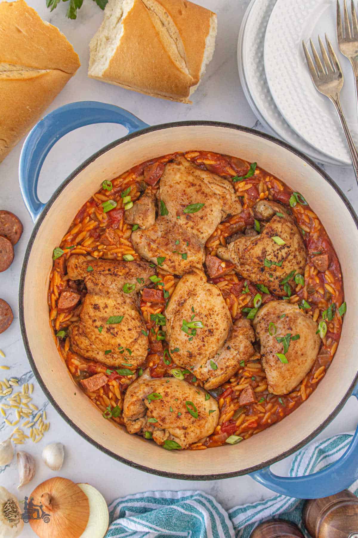 The finished Chicken and Orzo pasta recipe is in a Dutch Oven resting on a table with bread chunks near the pot's handle.