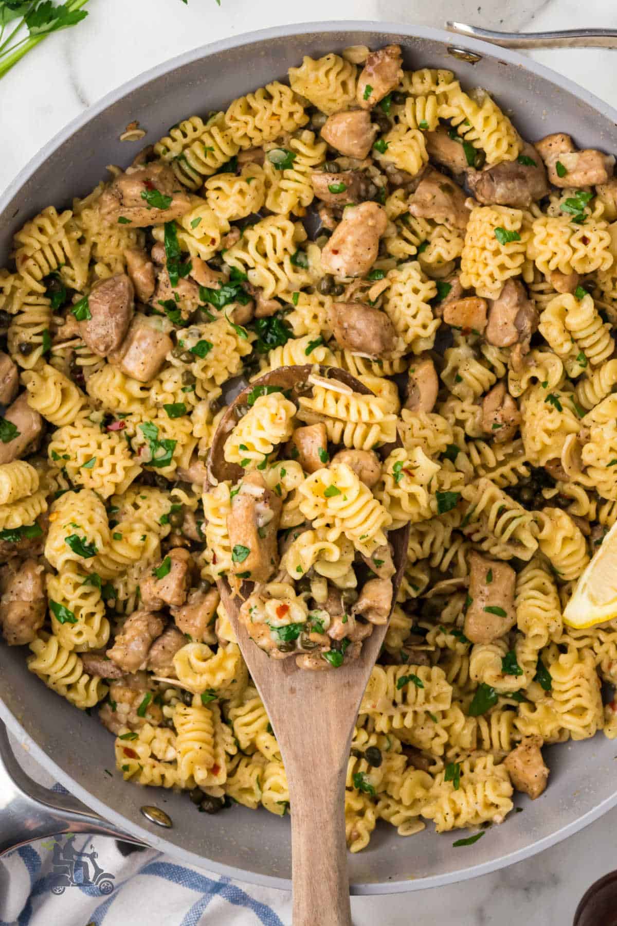 A wooden serving spoon scoops up some of the completed chicken thigh piccata dish. 