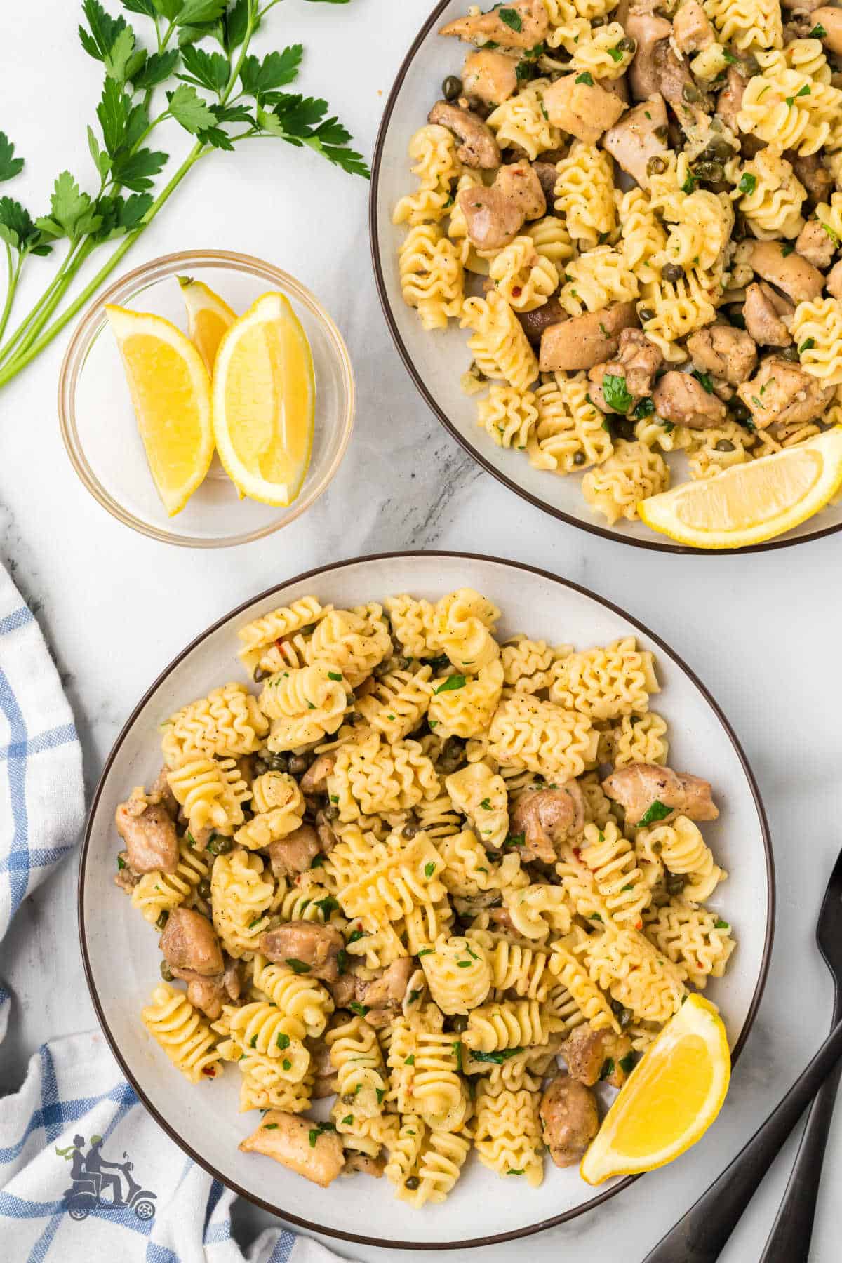 The one-skillet chicken pasta piccata dish is served on two white serving plates. 