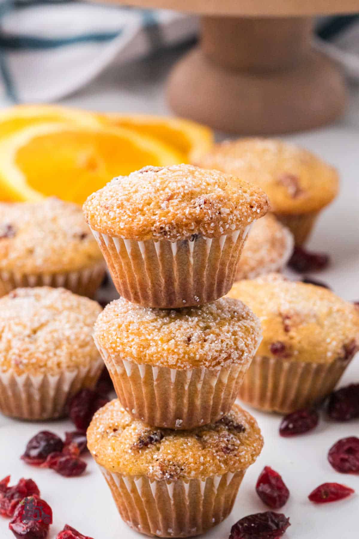 Three orange cranberry spice muffins with sugar toppings are stacked on each other.