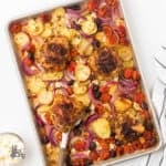 Greek chicken thighs are prepared in a sheet pan with vegetables.