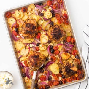 Greek chicken thighs are prepared in a sheet pan with vegetables.