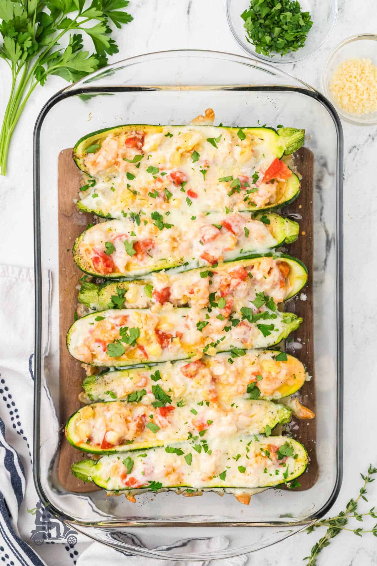 A baking dish holds baked shrimp stuffed zucchini boats sprinkled with parsley and Parmesan cheese.