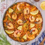 Shrimp and rice are made as an easy recipe shown in a large skillet, garnished with fennel fronds and lemon wedges.