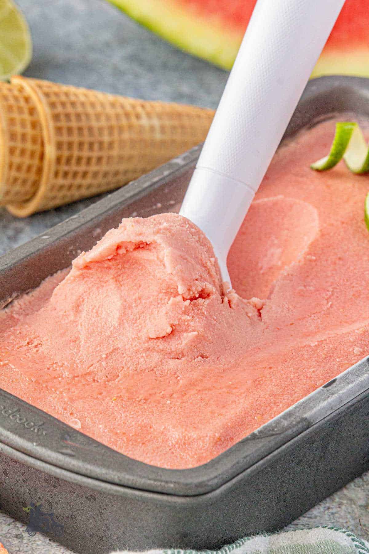 An ice scream scoop is scraping up a scoop of creamy watermelon ice cream.