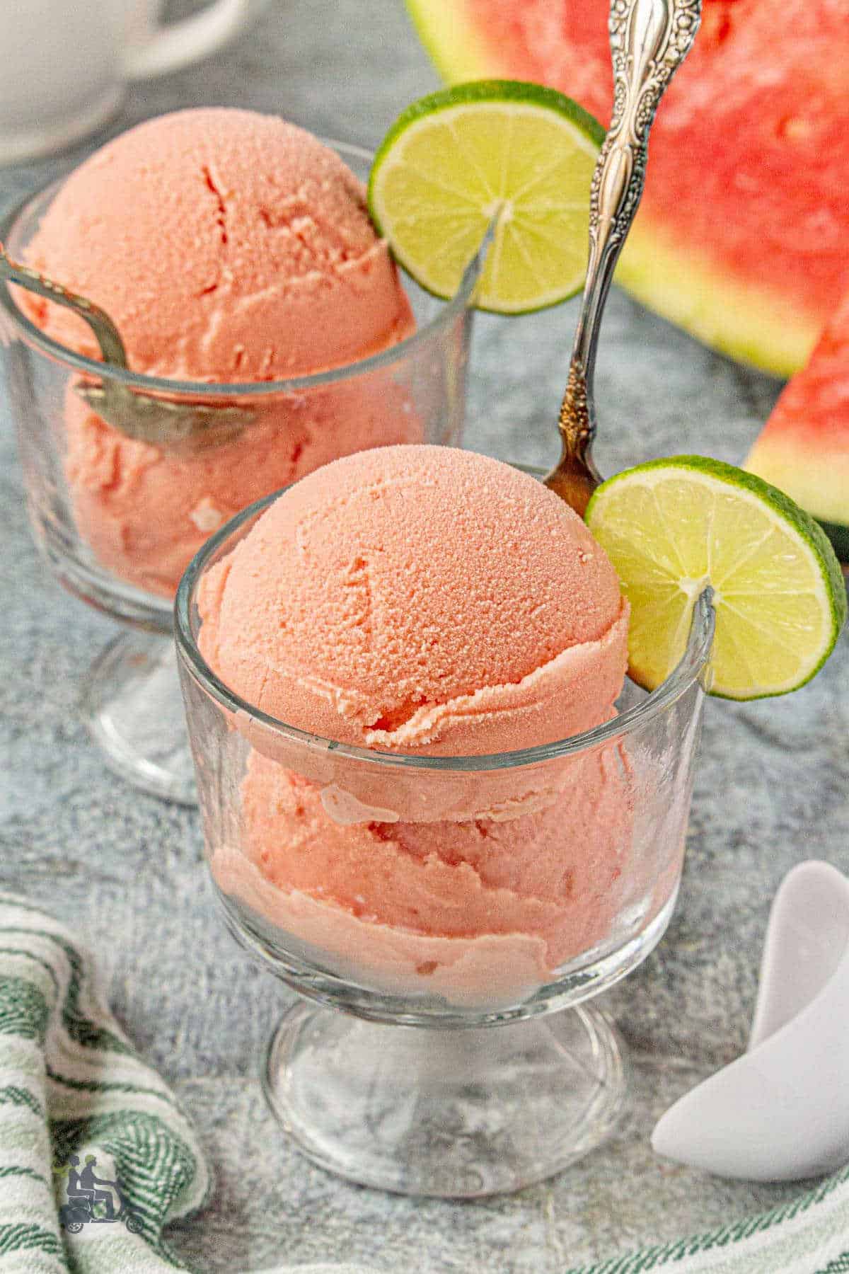 Two glass goblets hold watermelon ice cream with a wheel of lime on the side of the glass.