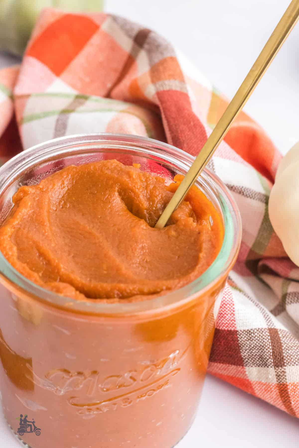 Creamy smooth pumpkin butter in a mason jar with a spoon stuck in the jar. 