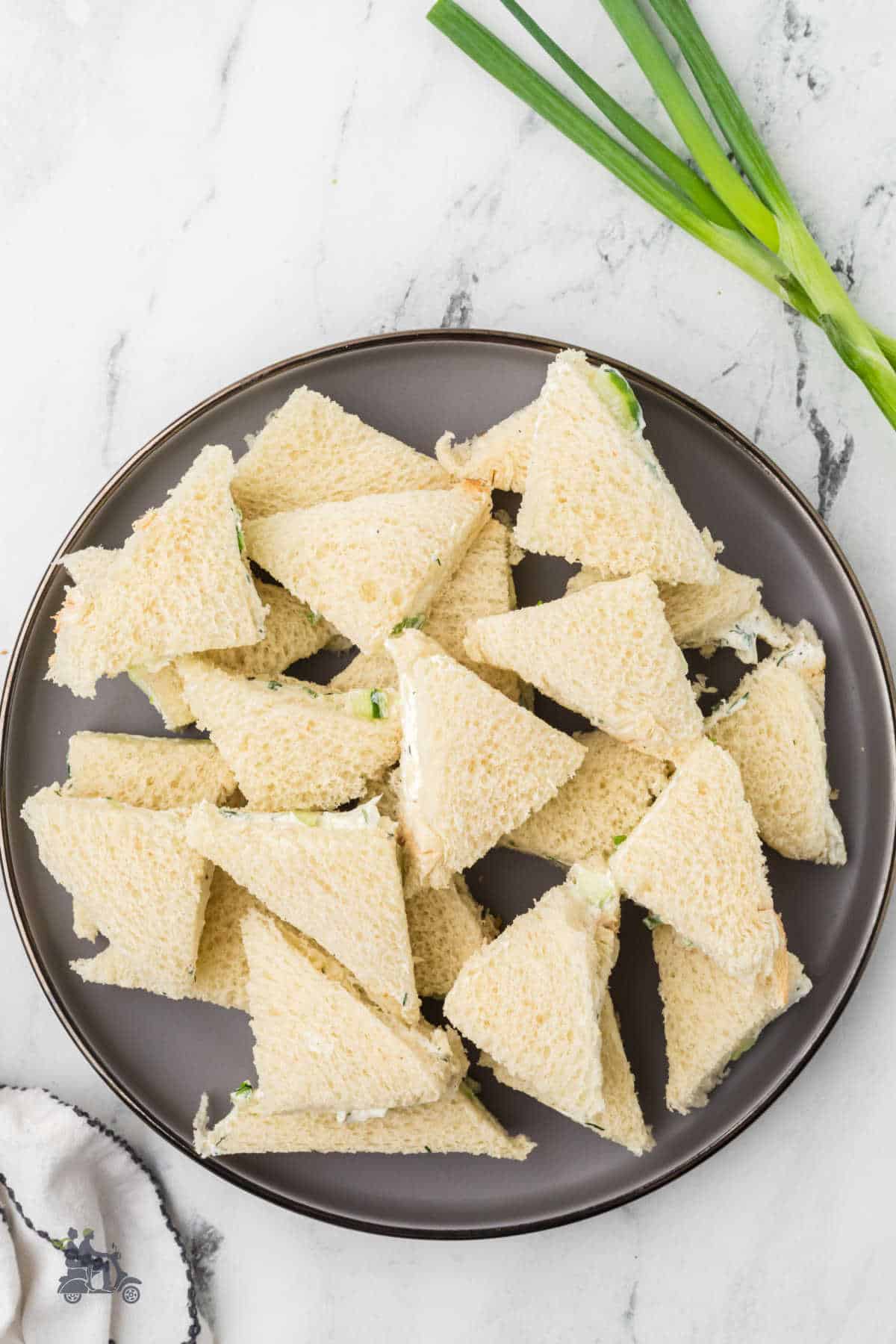 Cucumber tea sandwiches piled on a brown serving plate.