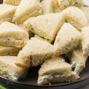 Benedictine cucumber tea sandwiches piled on a brown serving plate.