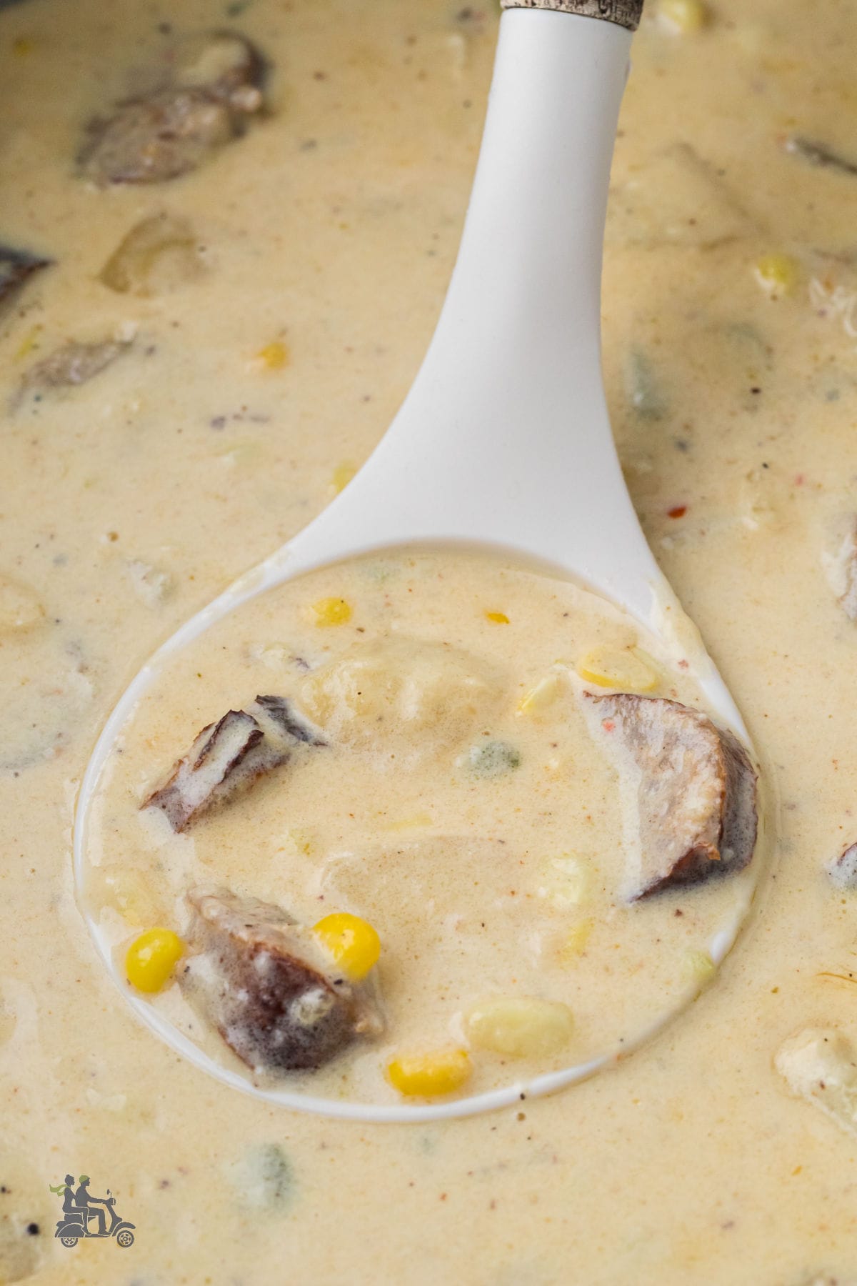 A ladle grabs a scoop of homemade corn chowder with fresh ingredients in a Dutch oven. 