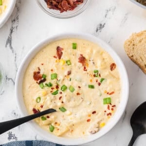 Overhead view of a bowl of creamy potato corn chowder with bacon bits and herbs on top.