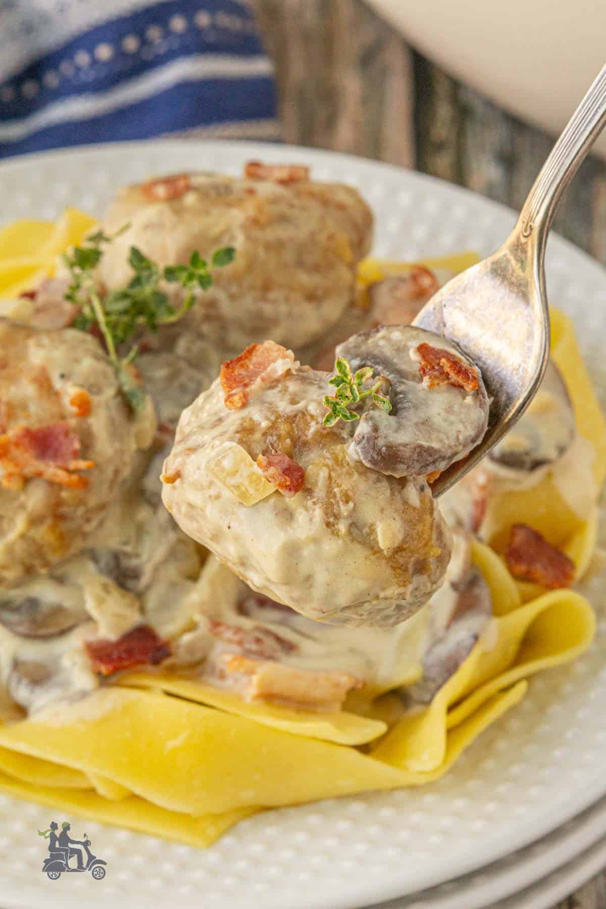 Coq au Vin Blanc Meatball on a fork with tagliatelle egg noodles on a white plate. 