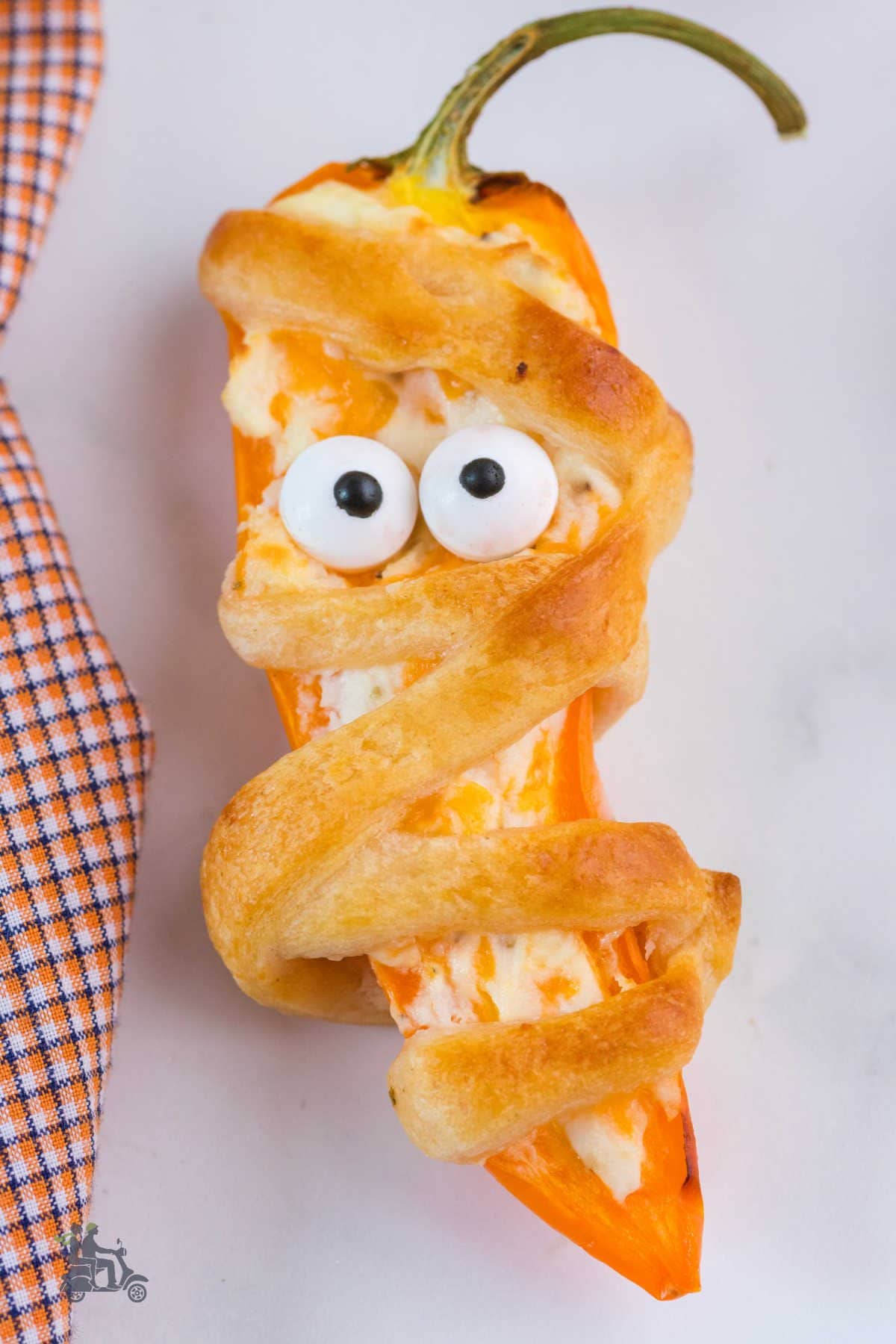 Close-up of a mini bell pepper cheese-stuffed and crescent dough- wrapped like a Halloween mummy 