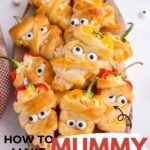 Cheese-stuffed mini peppers shaped like mummies on a wooden board with cute eyes staring out.