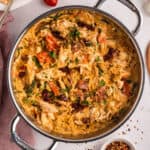 A deep skillet filled with Tuscan chicken and orzo pasta topped with fresh herbs.
