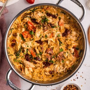 A deep skillet filled with Tuscan chicken and orzo pasta topped with fresh herbs.