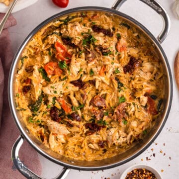 A deep pot filled with Tuscan chicken and orzo pasta, topped with fresh herbs.