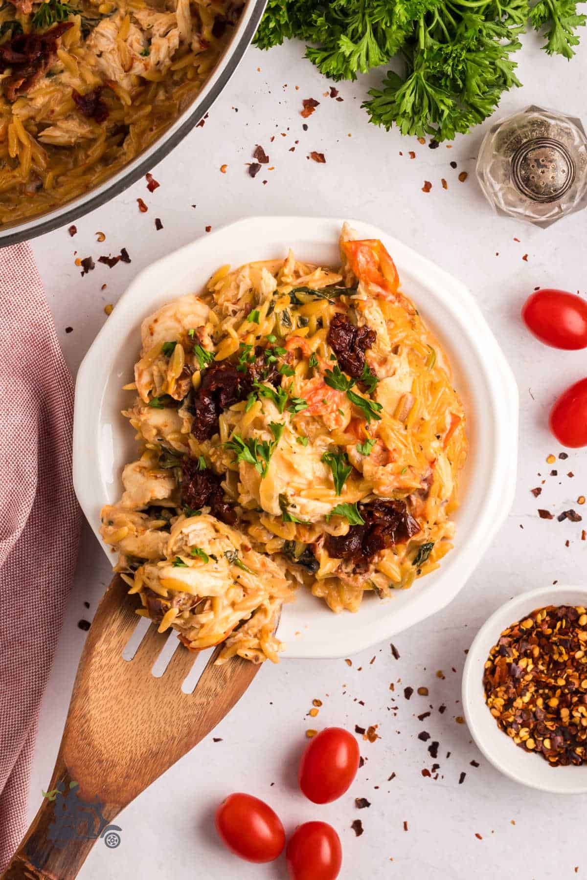 Wooden spoon places a serving of Tuscan chicken pasta with herbs and Parmesan cheese on a white plate.