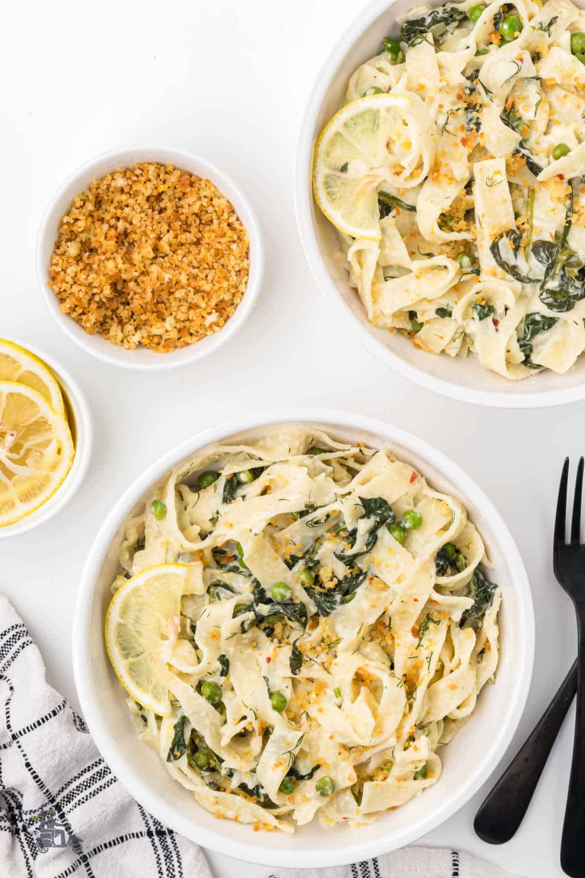 Two white bowls with an easy weeknight Mediterranean pasta dinner featuring creamy lemon spinach pasta with cream. 