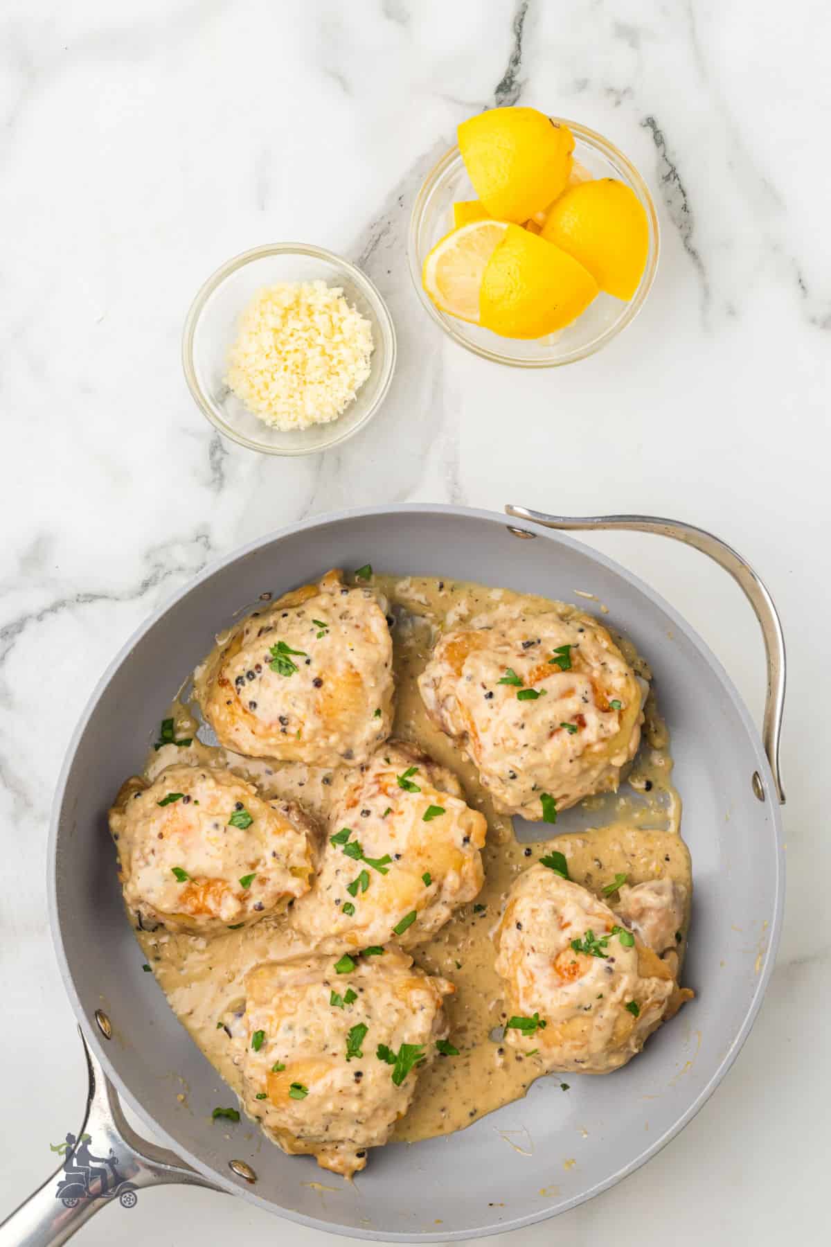 The completed skillet chicken thighs dinner recipe with extra lemon wedges and pecorino romano on the side.