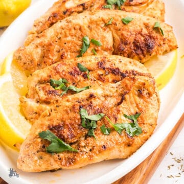 Greek Yogurt marinated chicken breasts on a white platter.