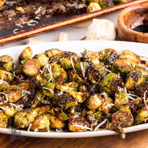 Crispy Brussels sprouts topped with grated Parmesan cheese and Balsamic glaze on a white platter.