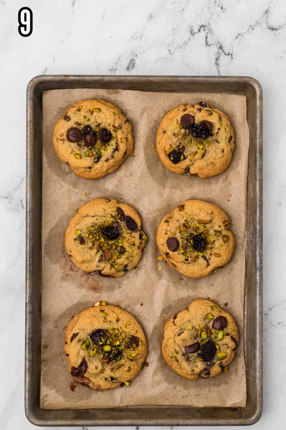 Pistachio cherry chocolate cookies on a parchment-lined baking sheet, baked to golden brown. 