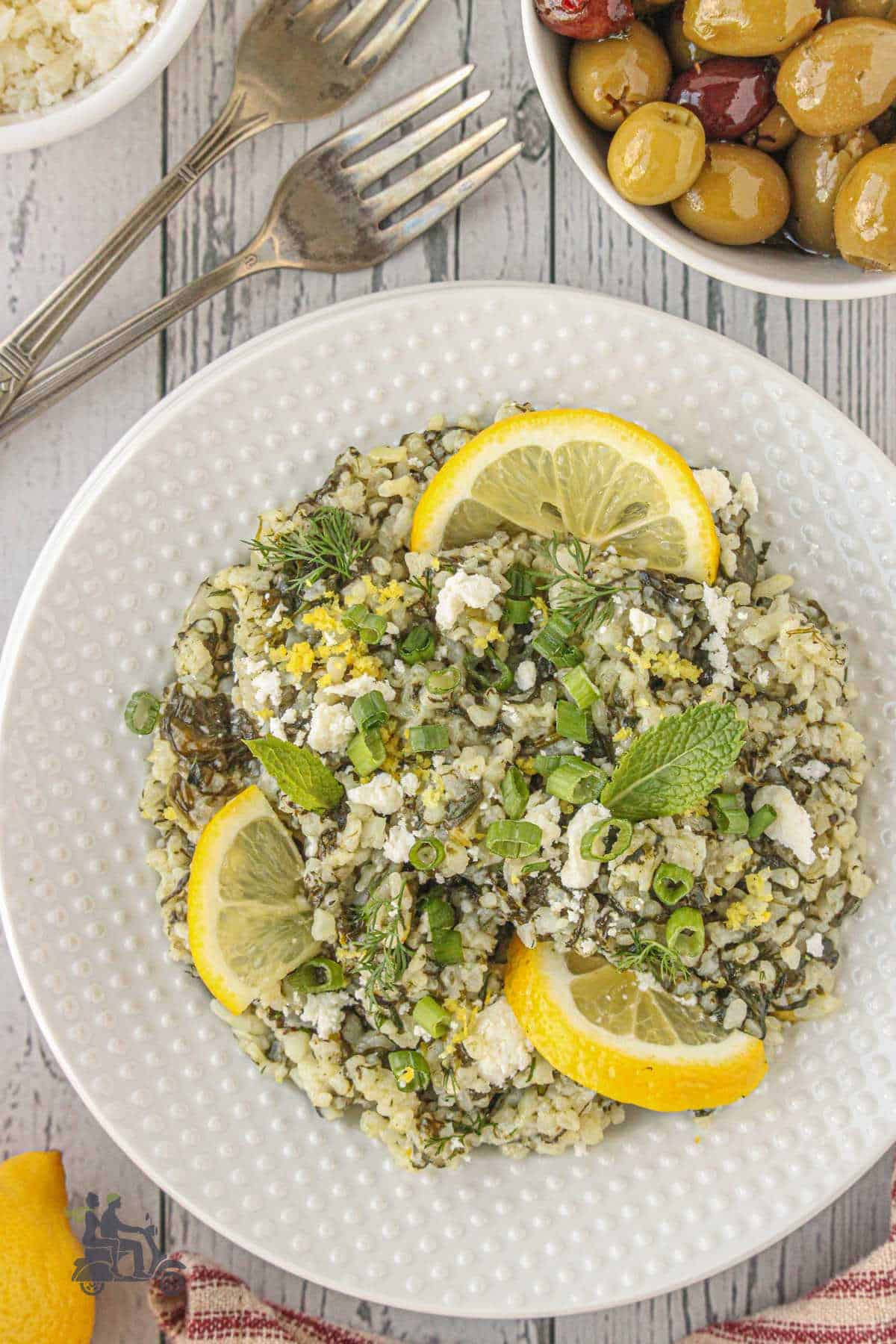 Overhead view of a white plate holding a serving of a spinach rice dish with lemon and herbs. 