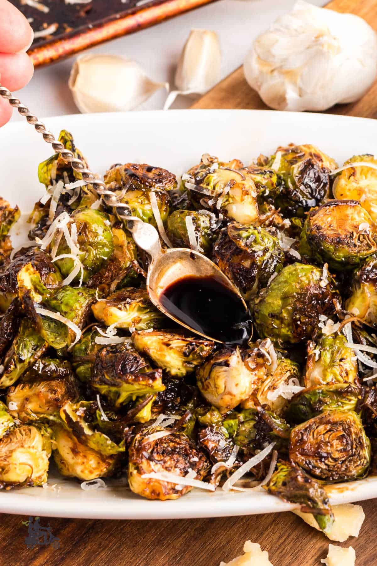 A spoon filled with reduced balsamic glaze is being poured over Brussels Sprouts. 