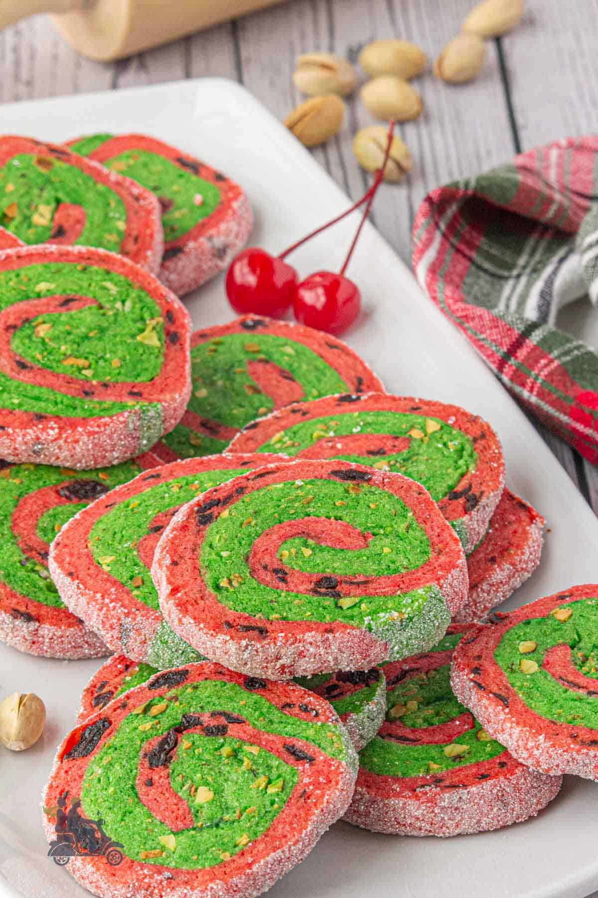 A White platter filled with colorful red and green spiral Christmas Cookies flavored with cherries and pistachios.