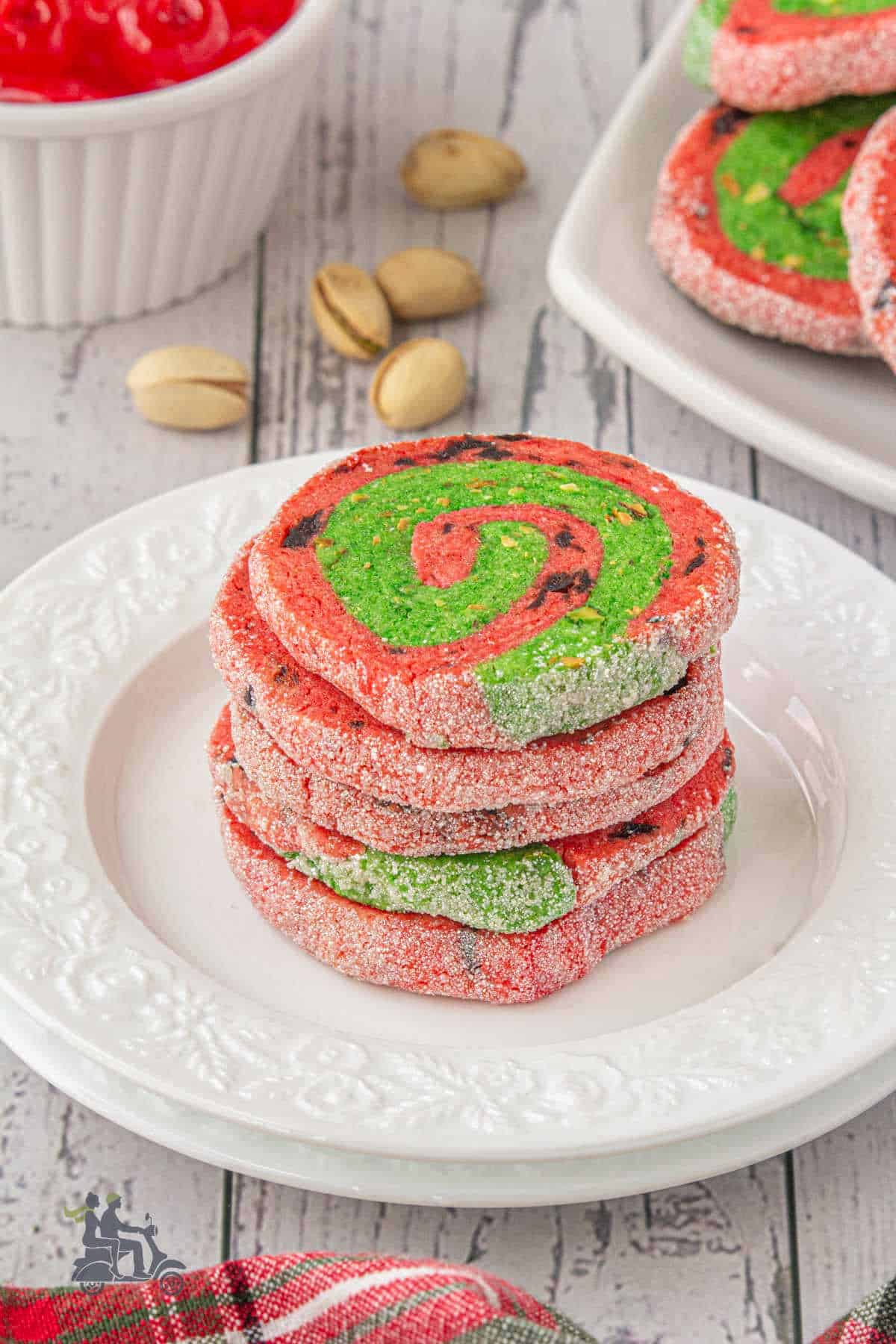 A stack of Christmas red and green pinwheel cookies on a white plate.